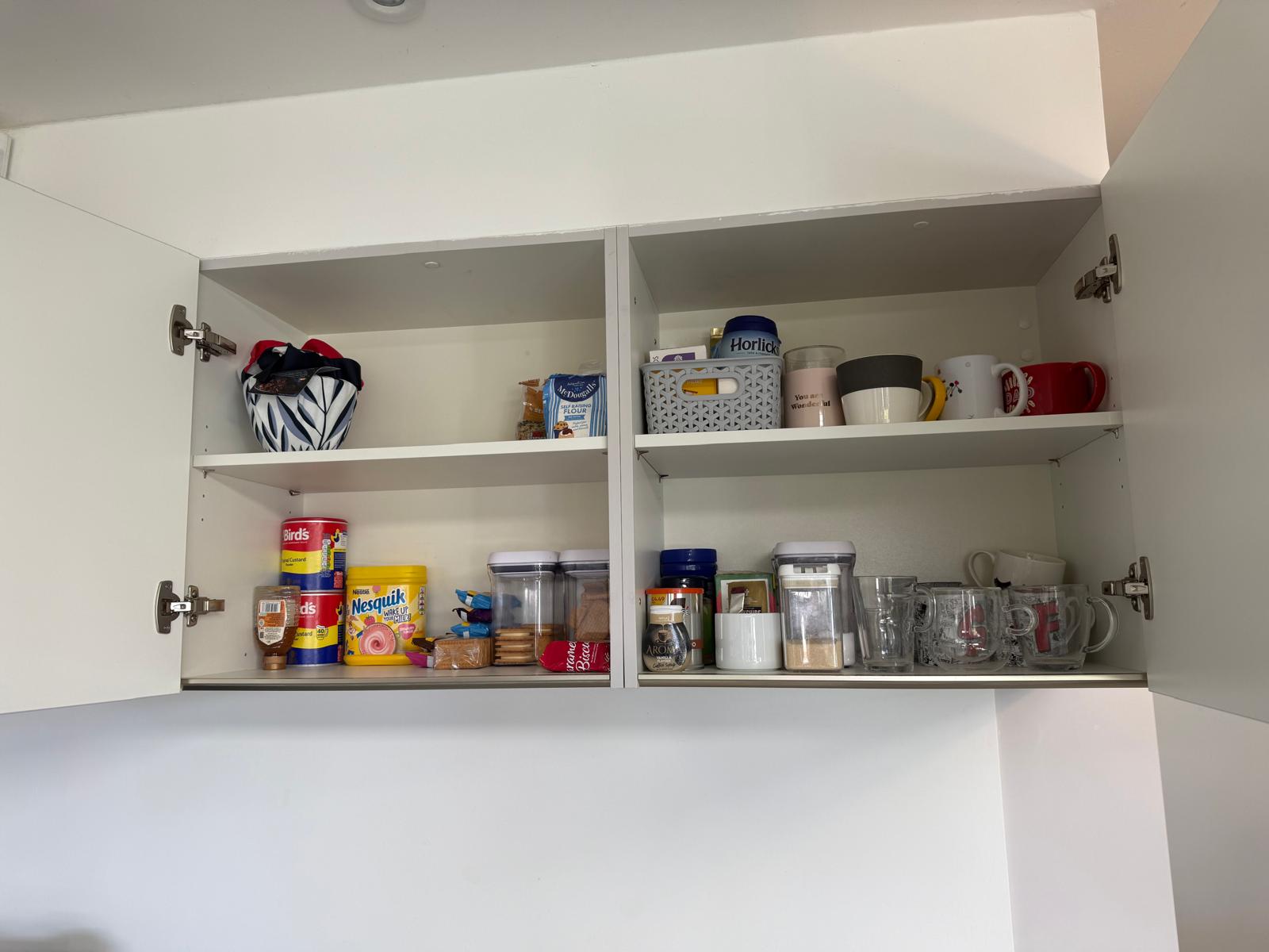 Organised kitchen cabinet with neatly zoned mugs, jars and baking essentials