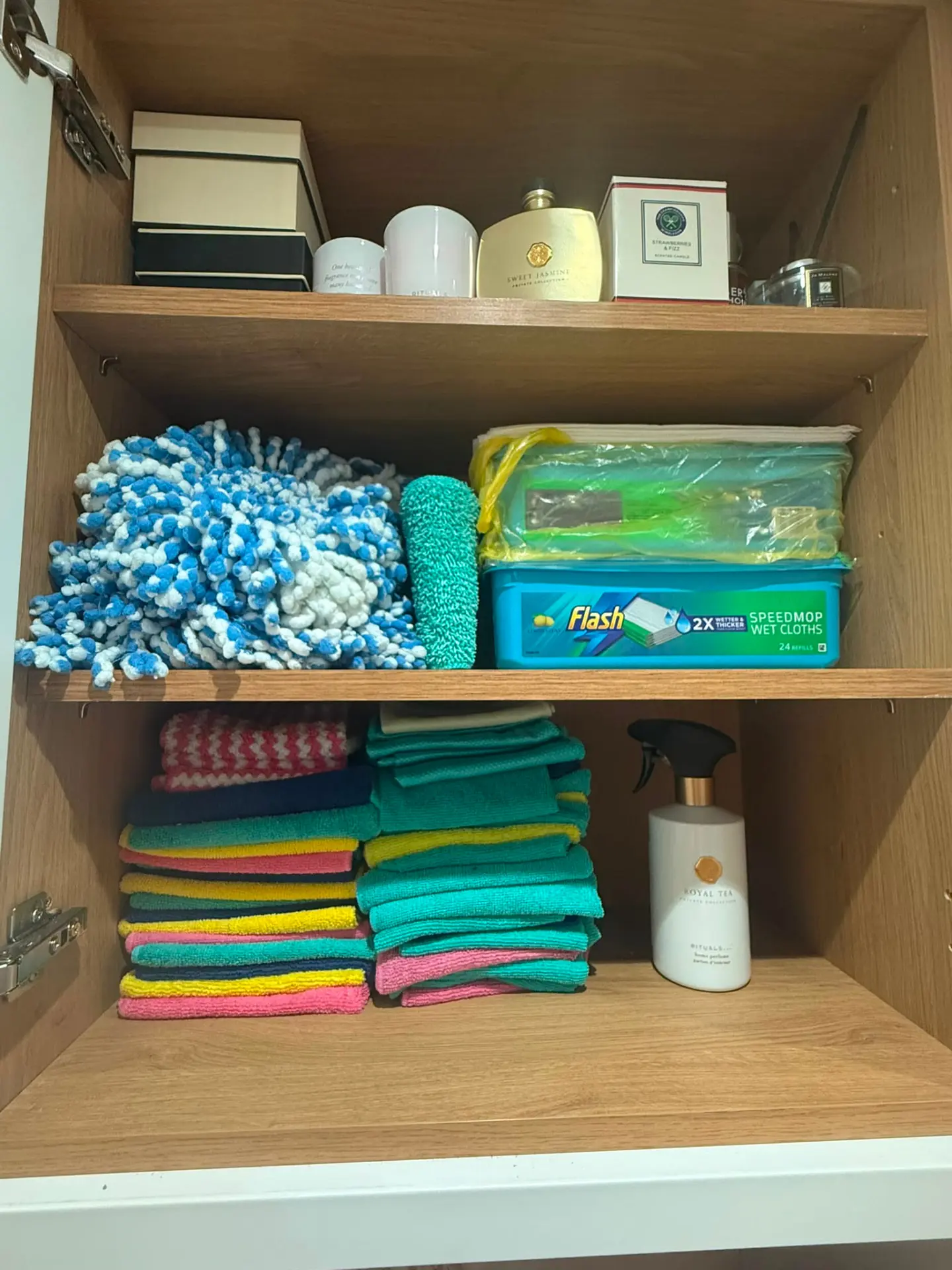 Organised cleaning cupboard with folded microfibre cloths and household products