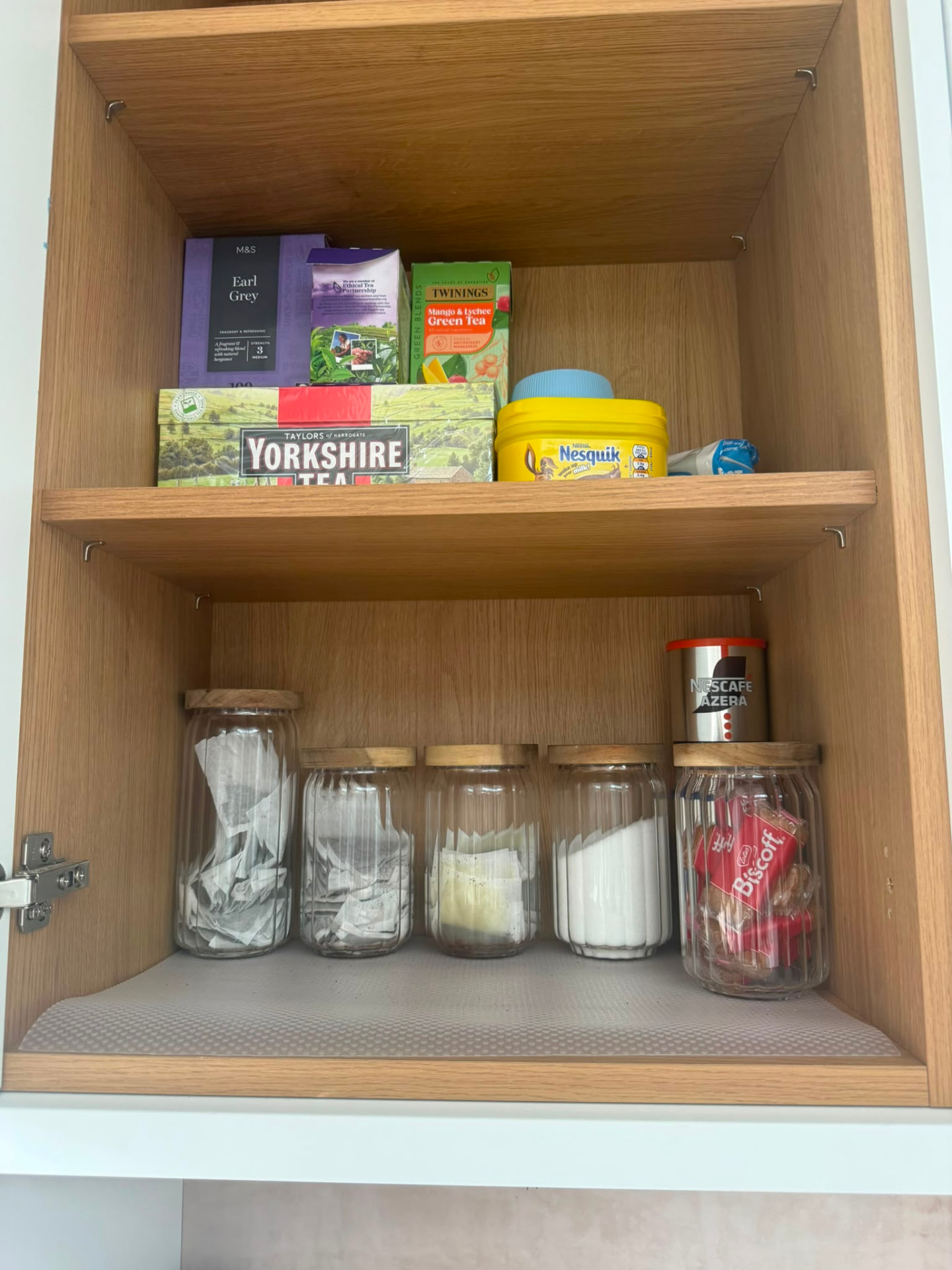 Oak kitchen cupboard organised with tea, coffee and airtight jars for sugar and biscuits on the lower shelf