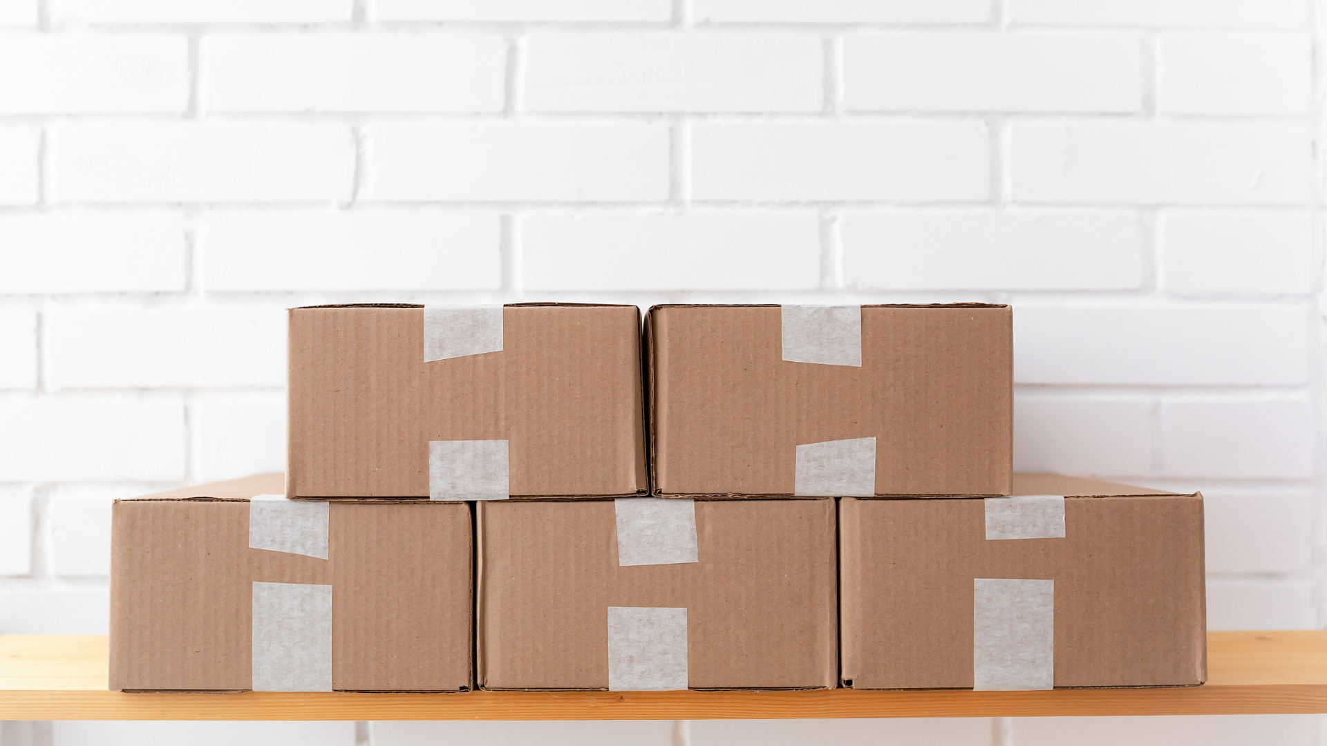 Neatly stacked and taped cardboard boxes ready for removal against a clean white brick wall