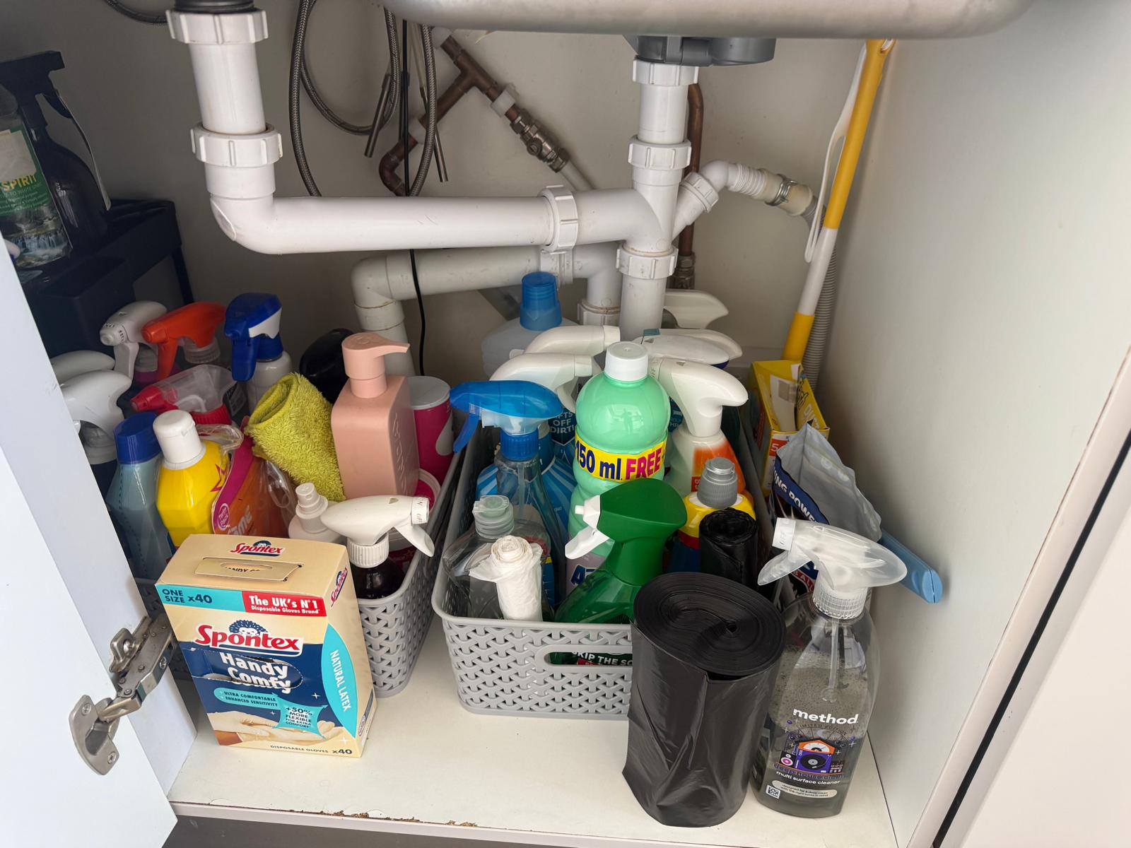 Under-sink kitchen cupboard packed with cleaning products before a professional reset