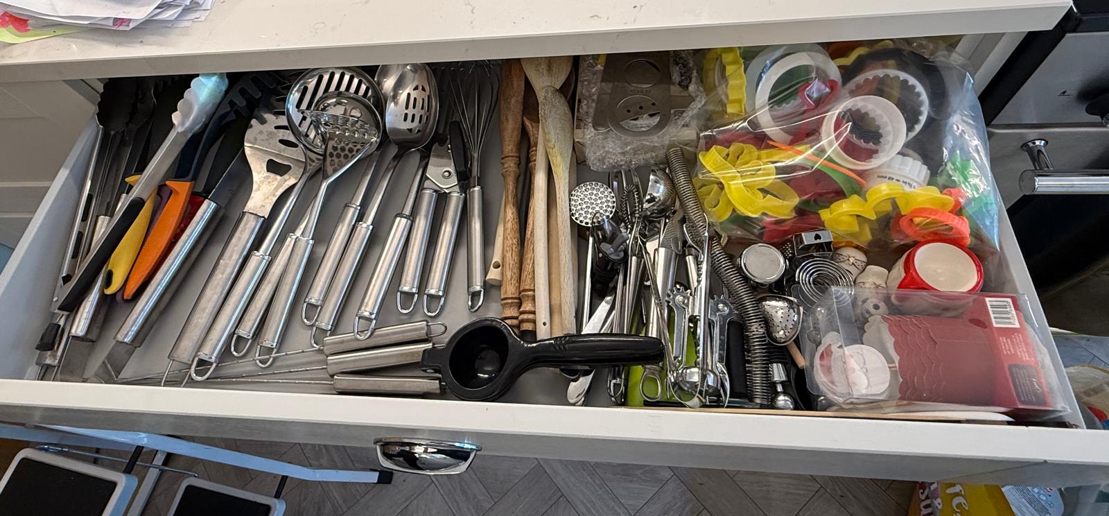 Overflowing kitchen utensil drawer packed with tools and cookie cutters before organisation
