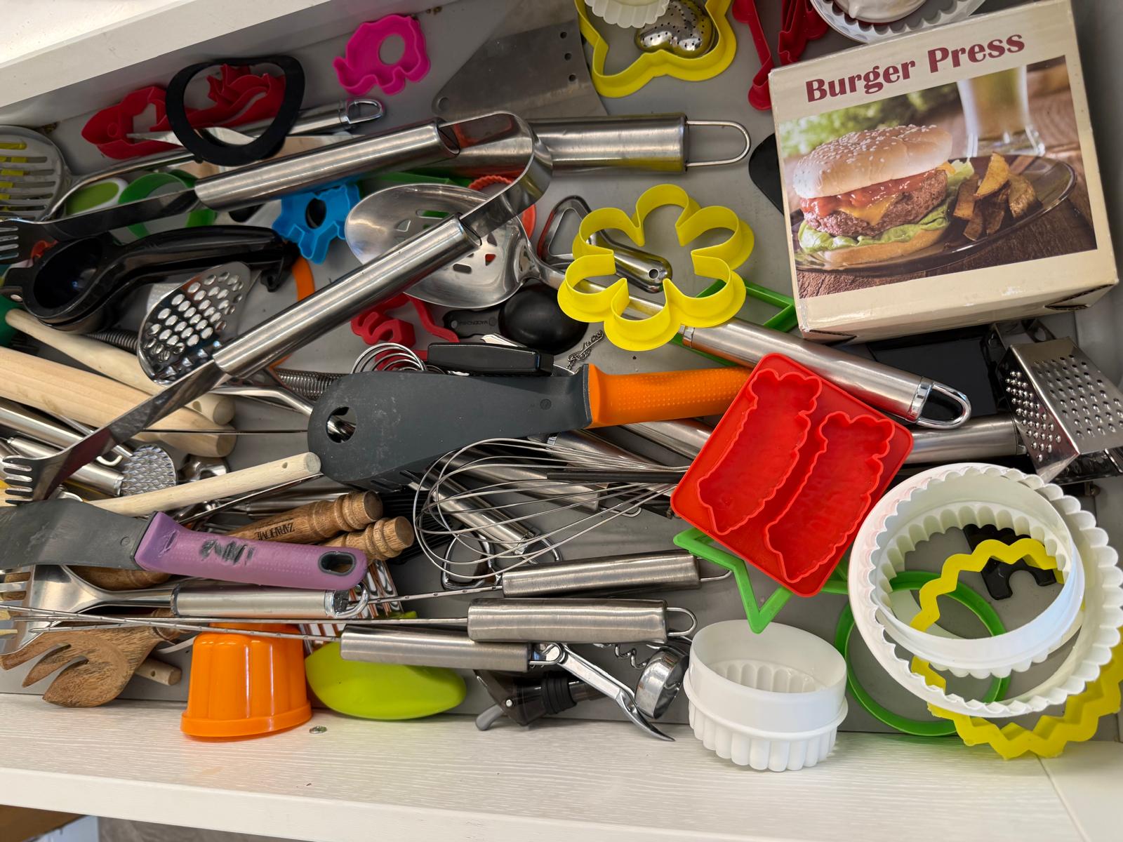 Chaotic top-down view of a kitchen utensil drawer overloaded with tools and gadgets