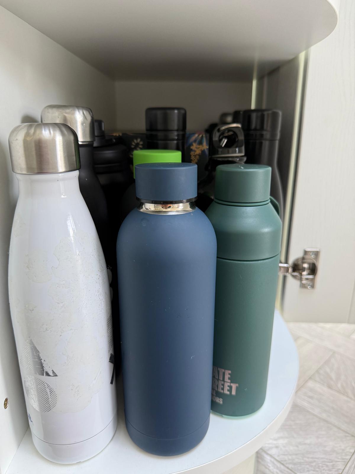 Reusable water bottles arranged neatly on a lazy Susan inside a kitchen corner cupboard