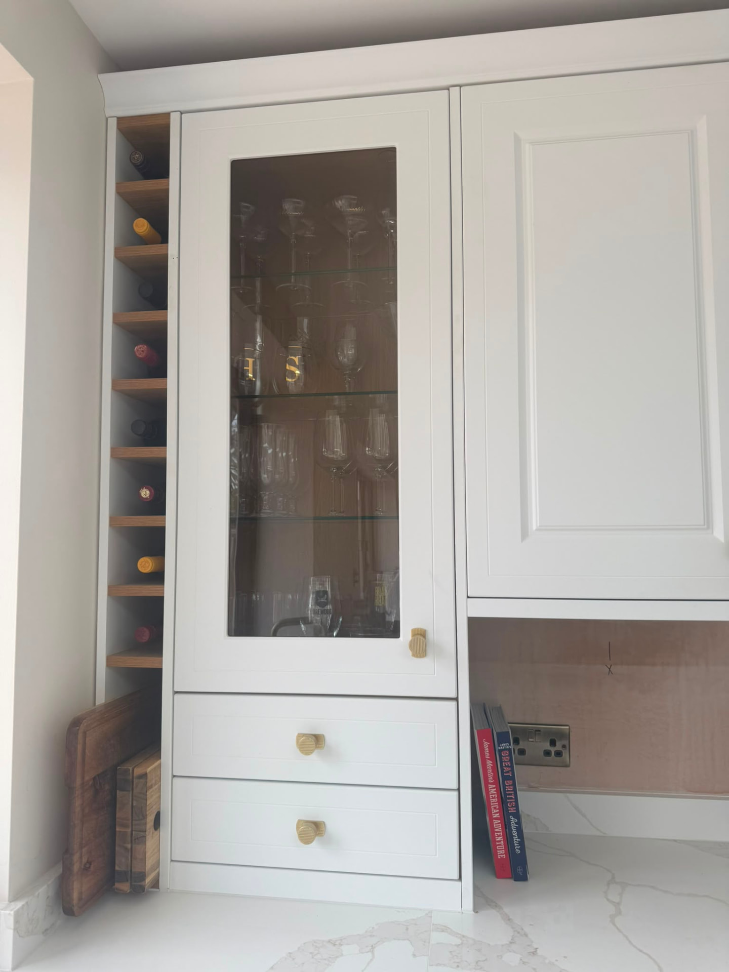Glass-fronted kitchen cabinet displaying organised glassware beside a built-in wine rack