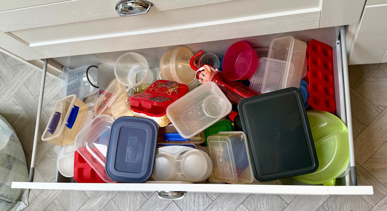 Cluttered Tupperware drawer stuffed with mismatched plastic containers before a kitchen reset