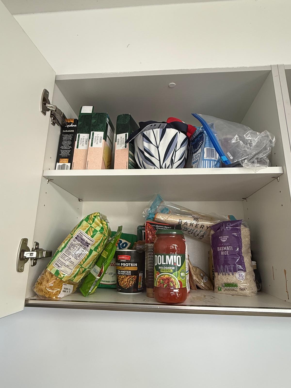 Disorganised kitchen pantry cupboard with pasta, rice and jars stacked without a system